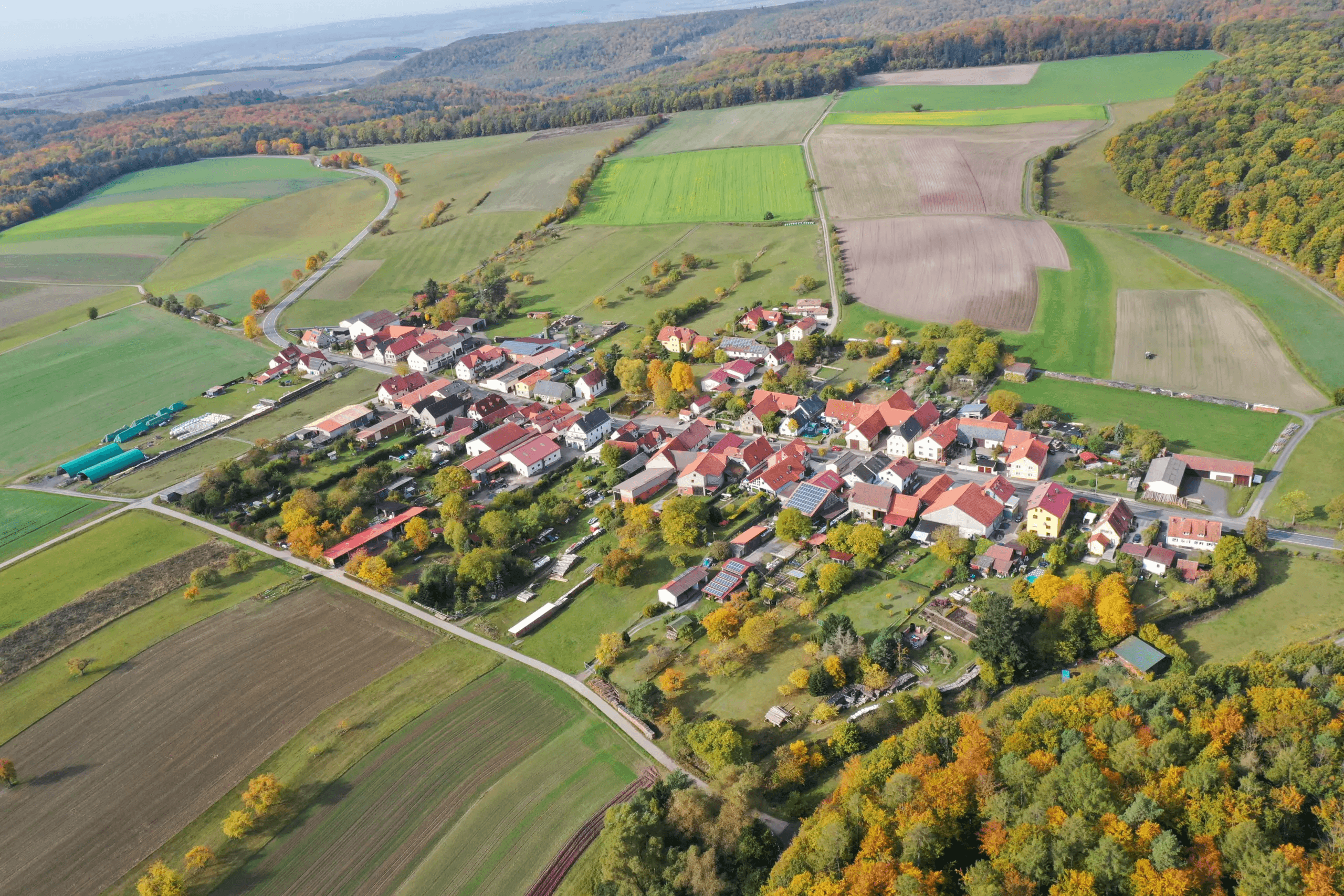 Luftbild von Hofstetten mit der langgestreckten Dorfstraße, umgebenden Feldern und dem bewaldeten Ortsrand